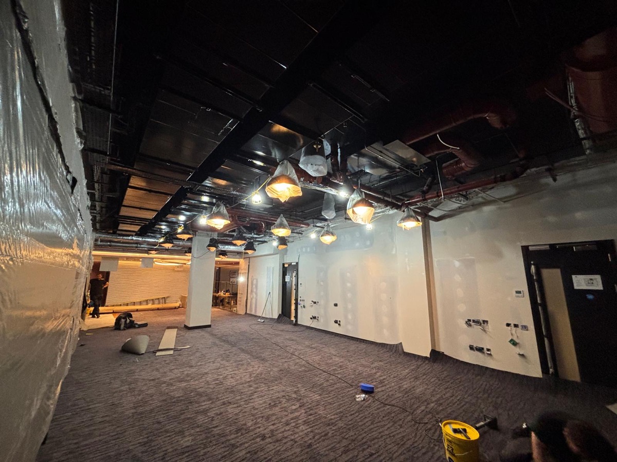 Fit-out space with exposed black ceiling services and protected pendant lighting